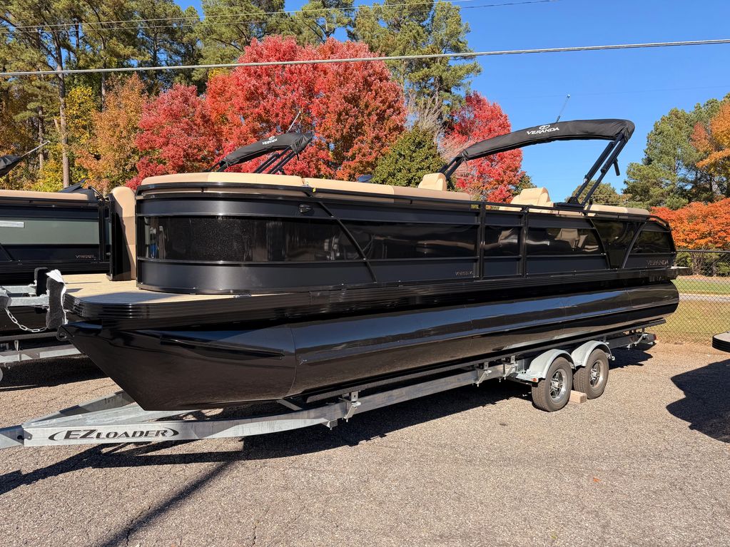Sleek black pontoon boat on trailer with autumn trees behind.