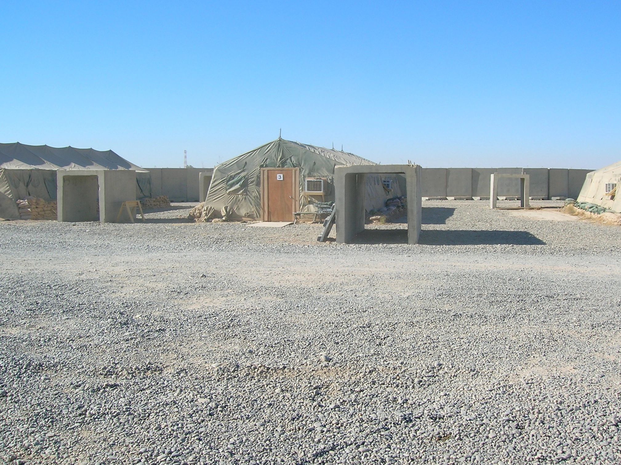 Military tents and barriers in a desert camp under a clear blue sky.