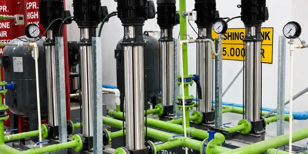 Industrial water pumps with green piping and pressure gauges in a mechanical room.