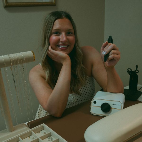 A smiling woman sitting at a table with jewelry and a Zapp device.