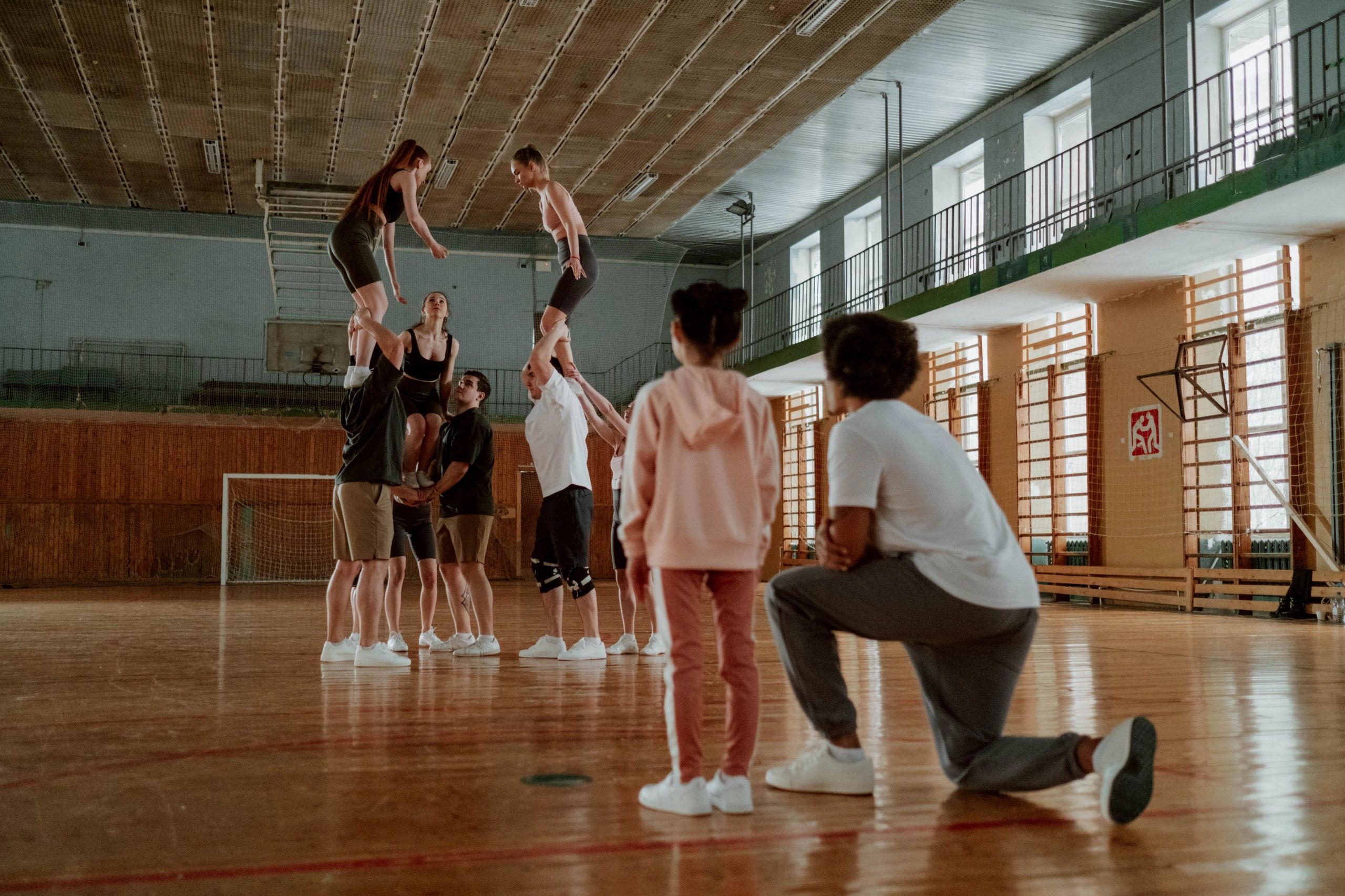 A kid with the coach is watching a cheer squad performing a routine. 