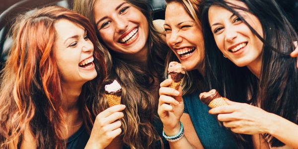 Four women huddled together eating ice cream cones and laughing
