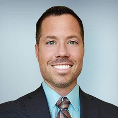 Smiling man in a suit and tie against a plain background.
