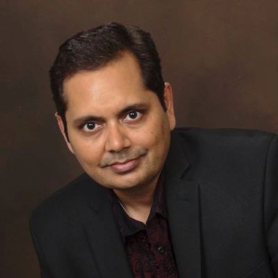 Man in a black blazer posing against a brown background.