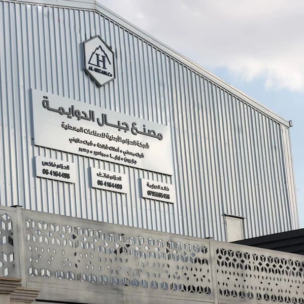 Exterior of a metal building with Arabic signage and a decorative fence.