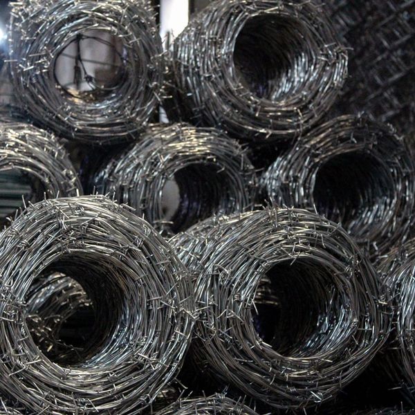 Rolls of shiny barbed wire stacked in a warehouse.