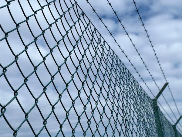 Close-up of a chain-link fence topped with barbed wire against a cloudy sky.