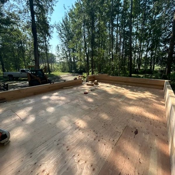 Plywood floor of unfinished wooden deck construction in a forested area.