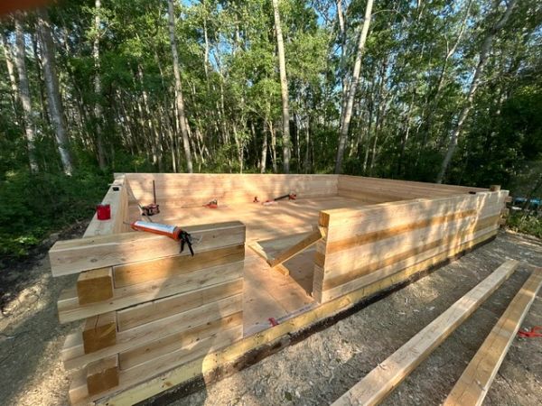 Wooden structure being built in a forest clearing.
