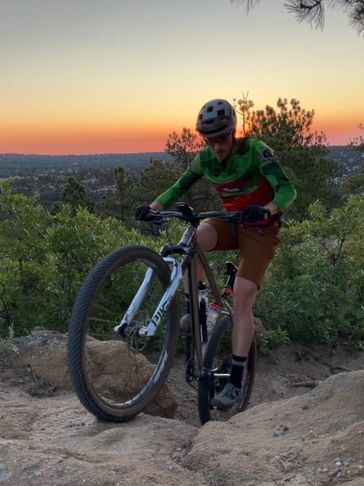 Cyclist performing a wheelie on a rocky trail at sunset.