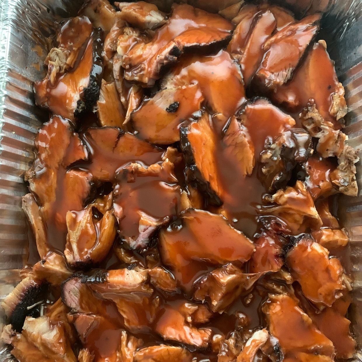 Barbecue smoked meat covered in rich brown sauce in a foil tray.