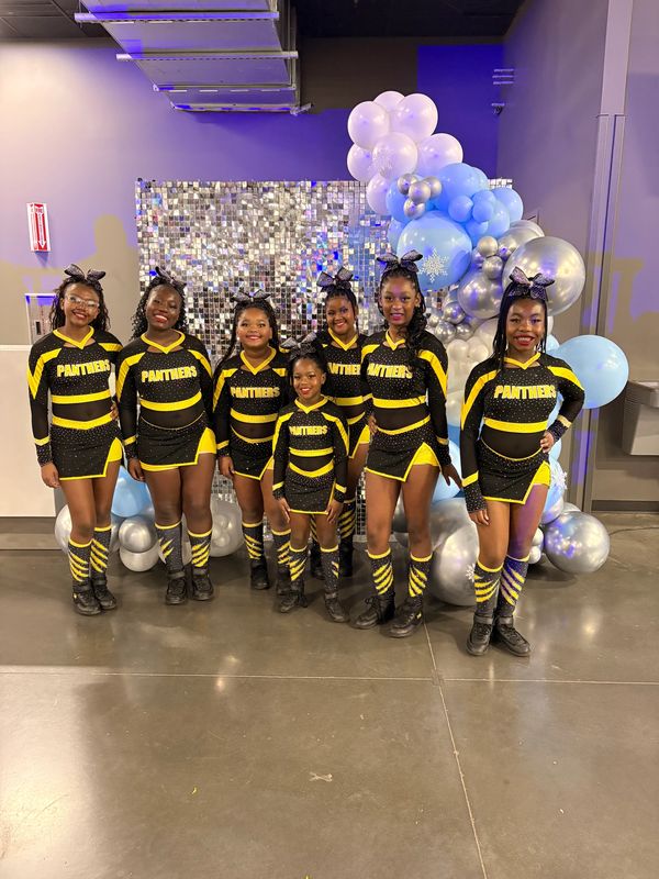 Six young cheerleaders in black and yellow Panthers uniforms pose with balloons.