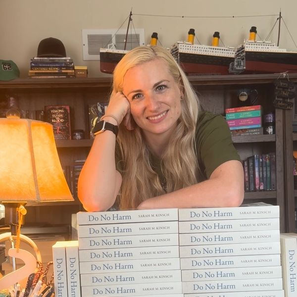 Author posing with multiple copies of her book "Do No Harm" in a cozy room.