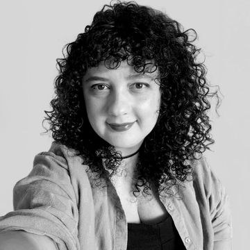 Mulher sorridente com cabelo encaracolado e blusa casual.