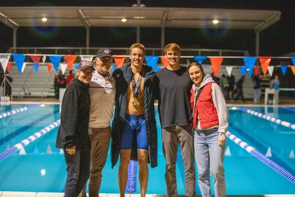 Group photo by a swimming pool with a swimmer wearing medals.