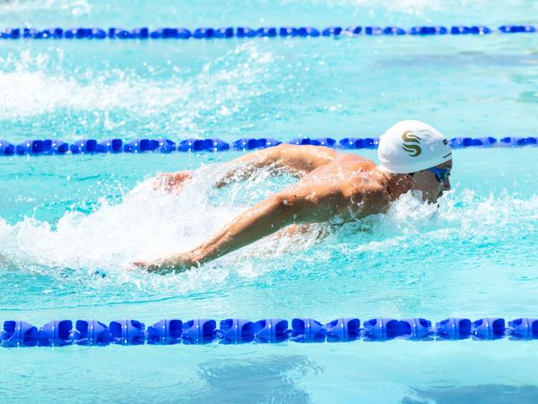 Swimmer in white cap doing butterfly stroke in pool.