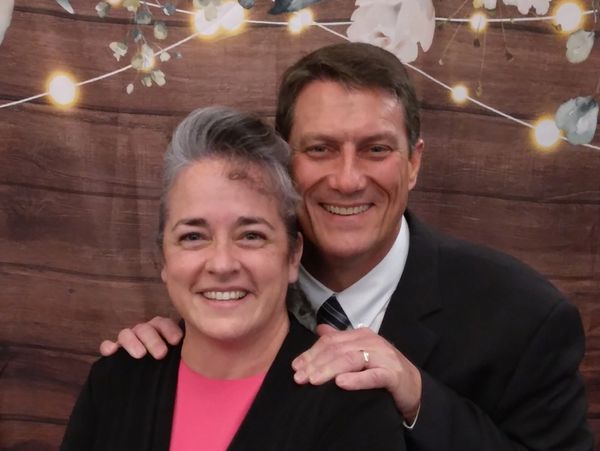 Smiling couple posing in front of wooden background with string lights.