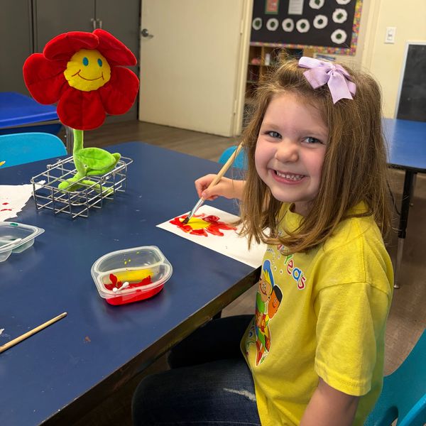 Smiling girl painting a red flower.