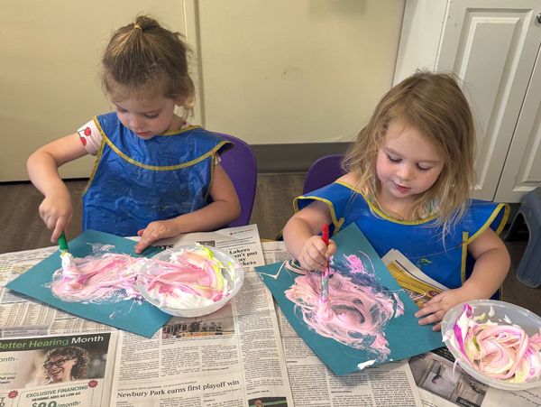 Two girls painting with pink and white colors on blue paper.