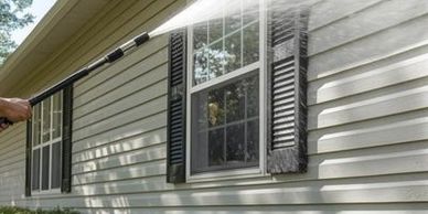 A person power washing the exterior siding of a house near windows.