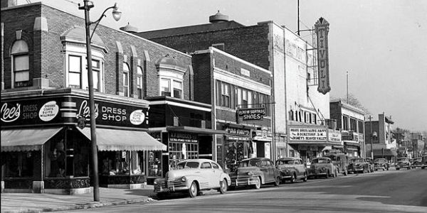 Historic street scene with vintage cars and stores.