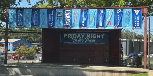 Stage at Clair Engel Park in Shasta Lake with Friday Night in the Park sponsor banners hanging .