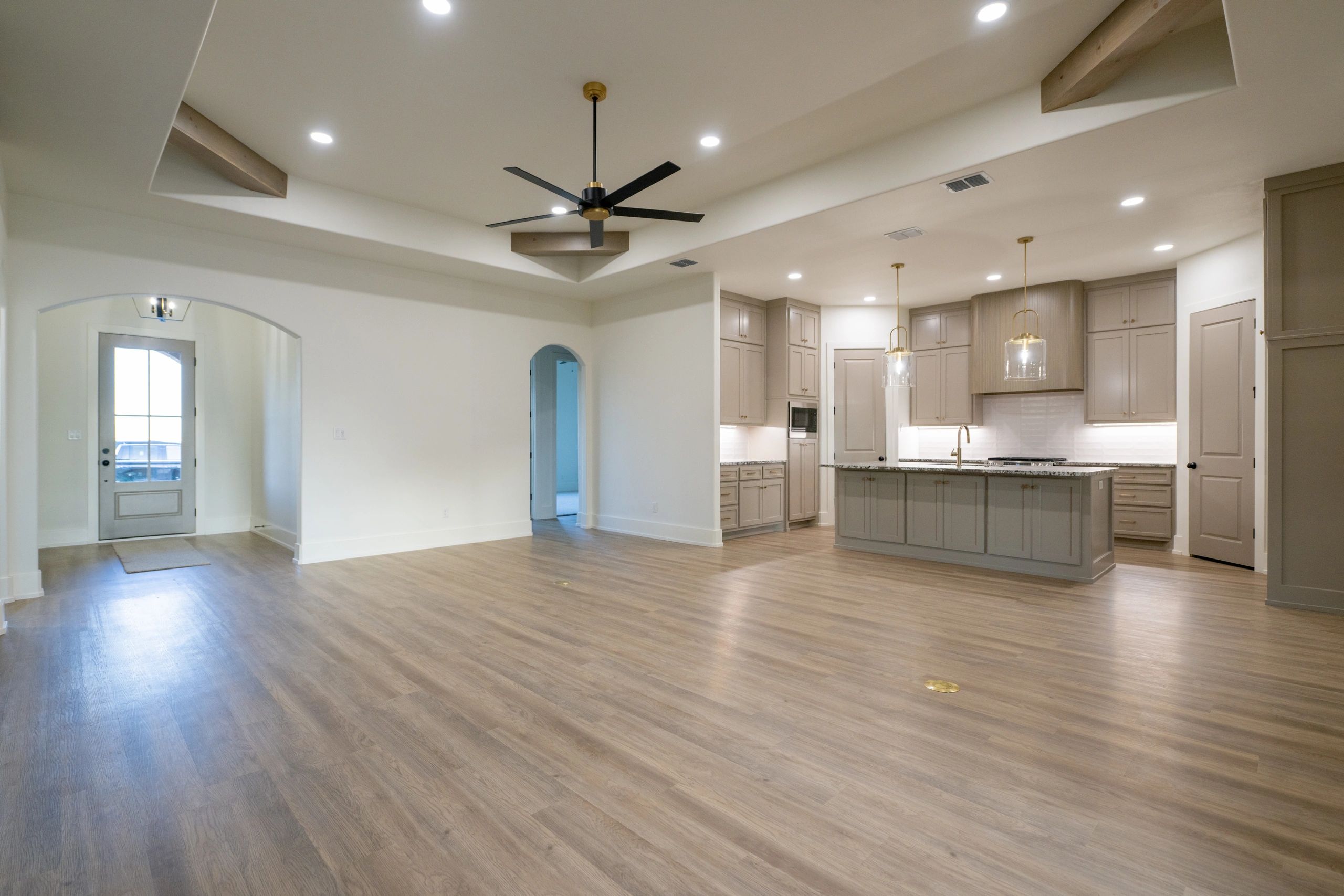 Modern open kitchen and living area with wood floors and ceiling fan.
