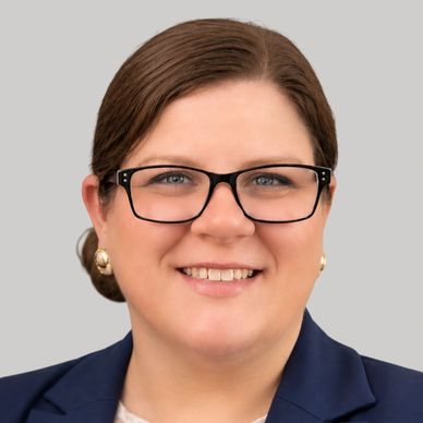 Smiling woman in glasses and a navy blazer.