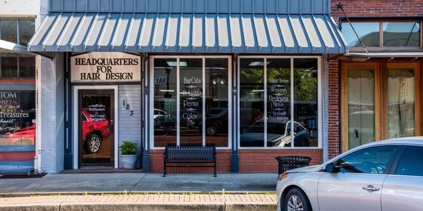 Front view of a hair salon named Headquarters for Hair Design with services listed on windows.