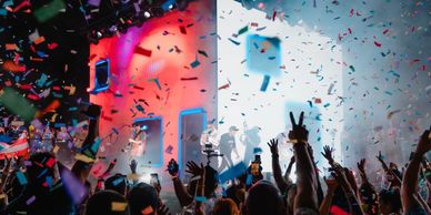 Crowd celebrates with confetti and raised hands at a vibrant event.