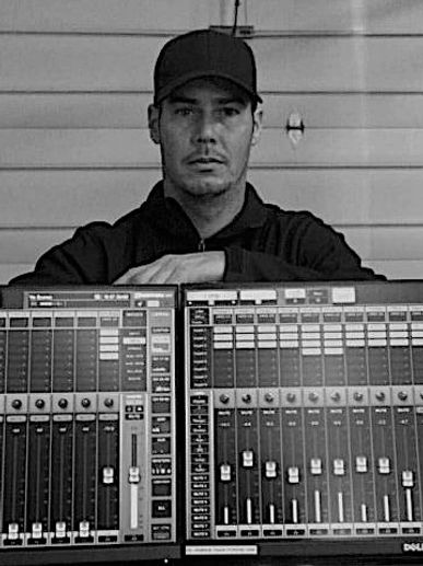 Man in cap standing behind audio mixing console.