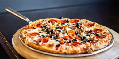 A freshly baked pizza topped with pepperoni, olives, and sausage on a wooden tray.