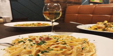 Creamy pasta with herbs and a glass of white wine on a restaurant table.
