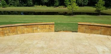 Stone patio overlooking a grassy field and pond with trees in the background.
