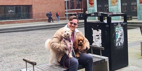 Man with two dogs sitting on a bench in an urban area.