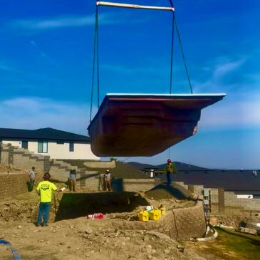A swimming pool being lifted into a backyard.