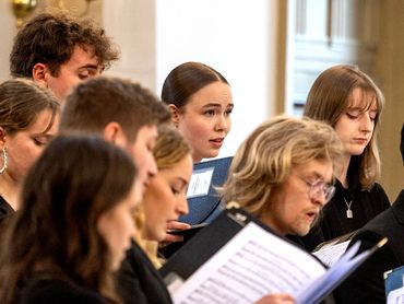A group of people singing in a choir, focused on their music sheets.
