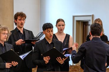 A group of young adults singing in a choir with a conductor.