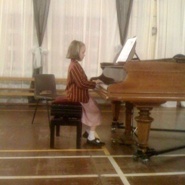 A young girl playing the piano in a school hall.