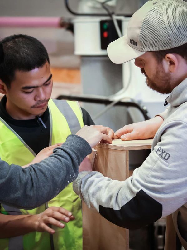 Three men collaborating on a woodworking project indoors.