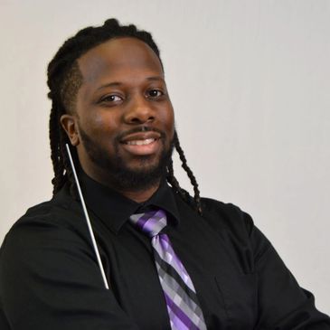 Smiling man with dreadlocks in formal attire.