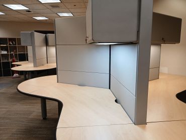 Empty office cubicles with wooden desks and gray partitions.