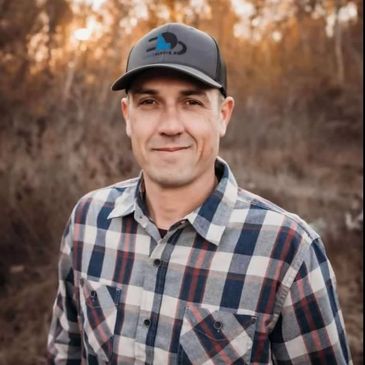 Man wearing a plaid shirt and cap outdoors in autumn.