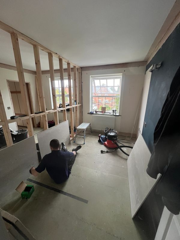 Person working on drywall installation in a room under renovation.