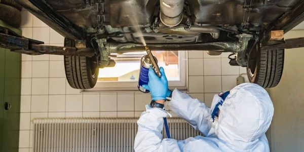Person in protective gear spraying under a car in a garage.