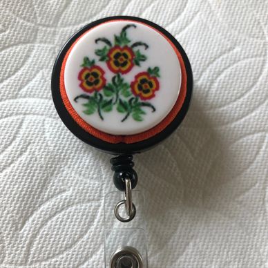 ID Badge reel has 3 pansy flowers with orange cording on black badge reel