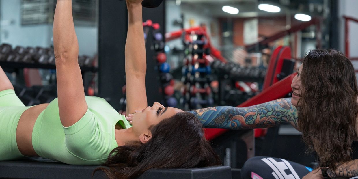 A woman in green works out with a trainer in a gym.