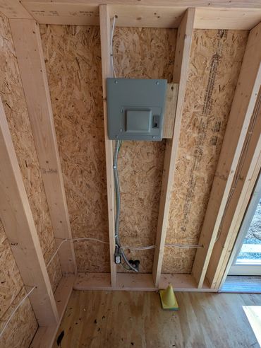 Electrical panel installed on wooden studs in unfinished room.