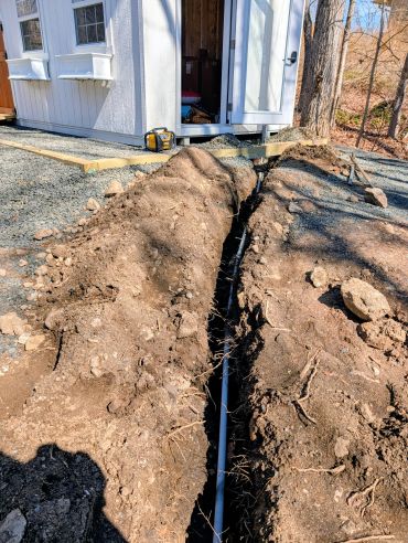 Trench with a pipe laid outside a small white building under construction.