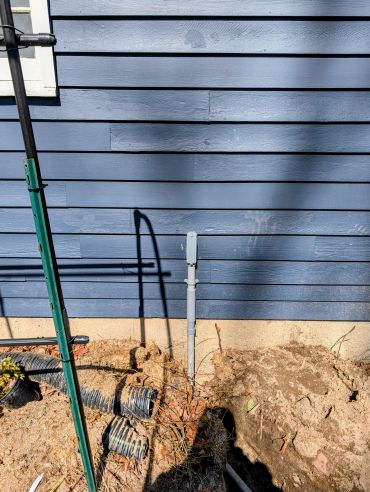 Blue house exterior with pipe and garden debris on the ground.